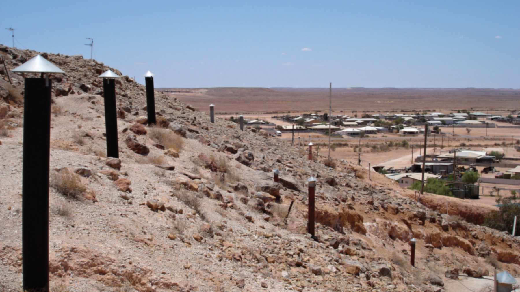 Vent pipes above underground homes on a rocky hillside in Coober Pedy, South Australia, with the town and desert behind