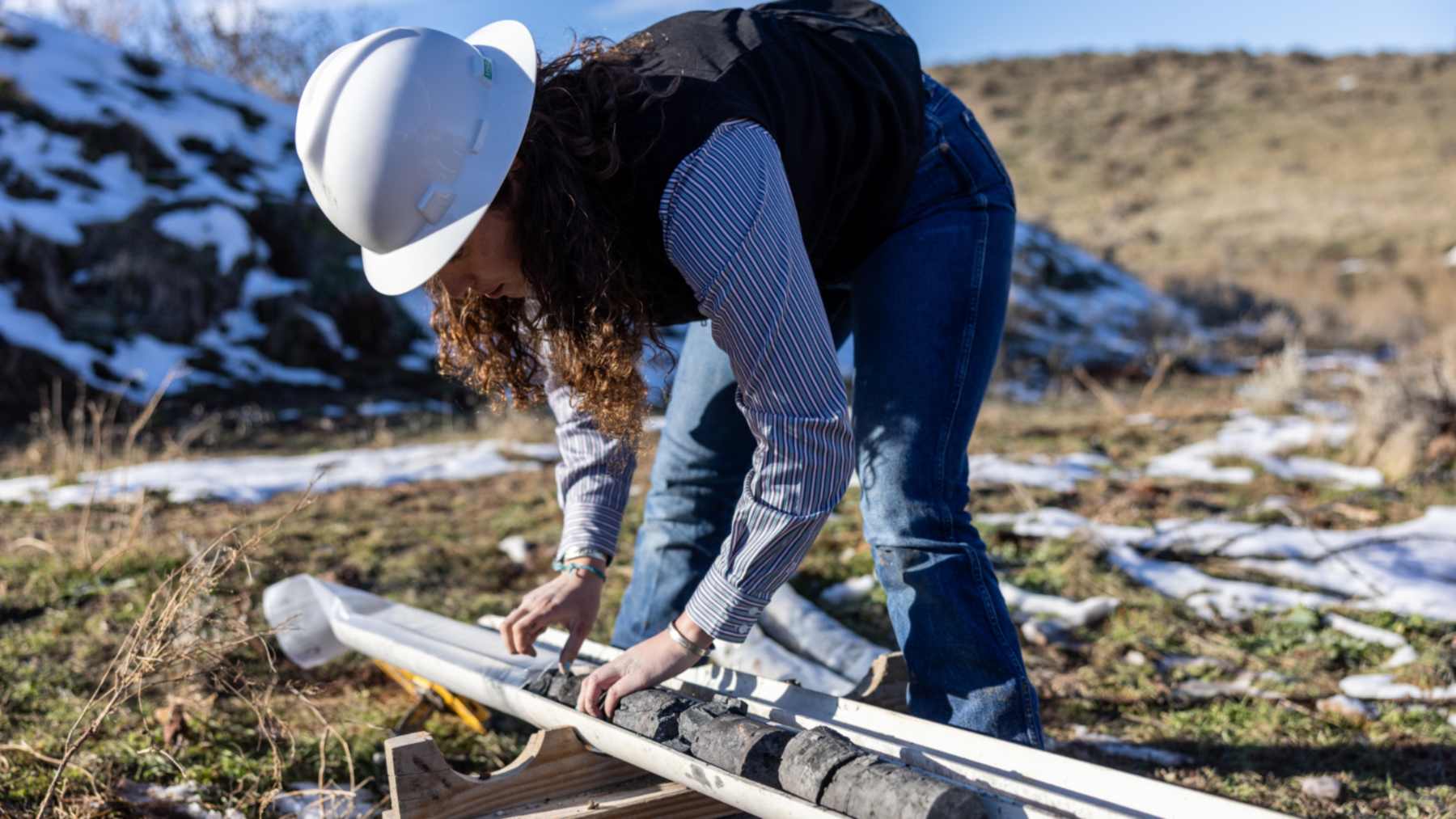 A worker in a white hard hat handles core samples in a field in Wyoming