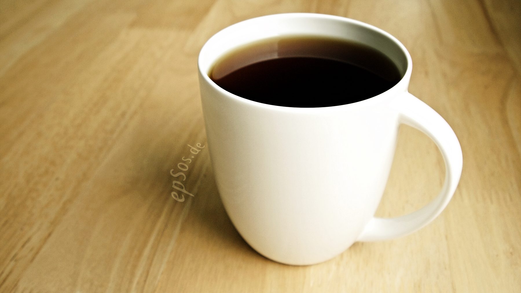 A white mug filled with black coffee on a wooden table