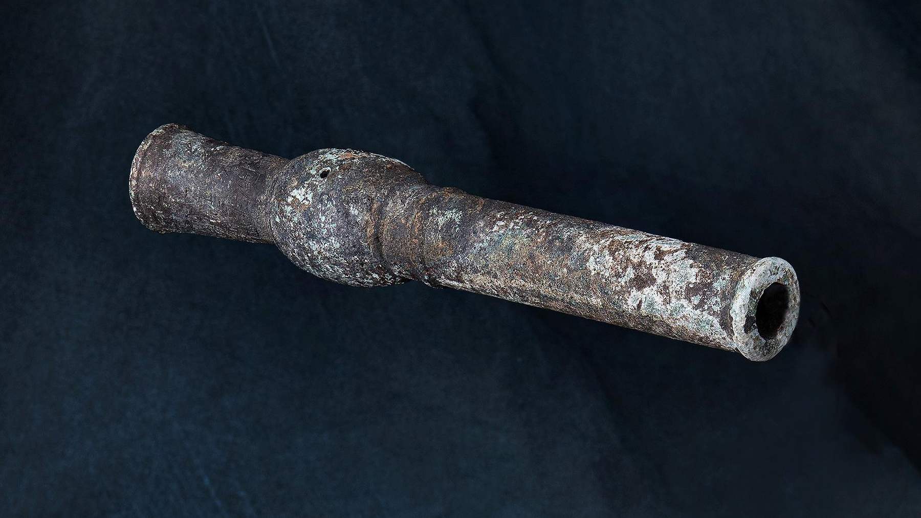The Hwangja Hwatong, a corroded bronze hand cannon, photographed against a dark blue background