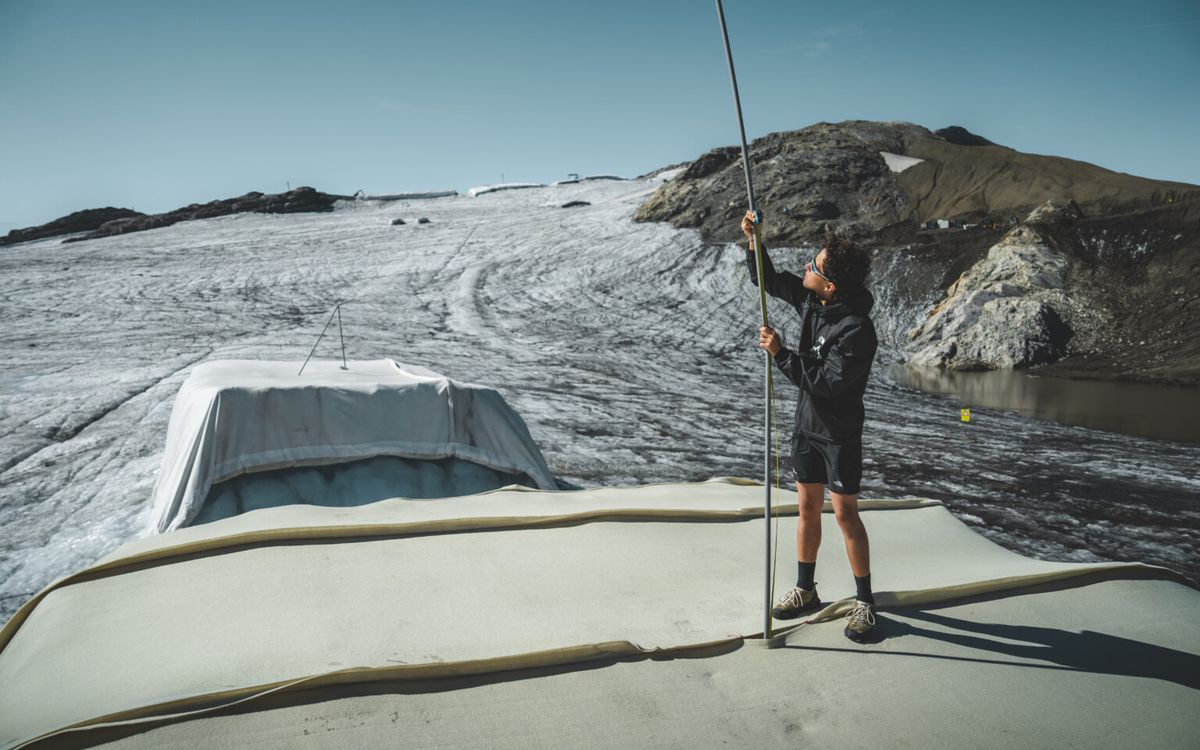 A team member holds a tall measuring stake on top of a cover at Glacier 3000