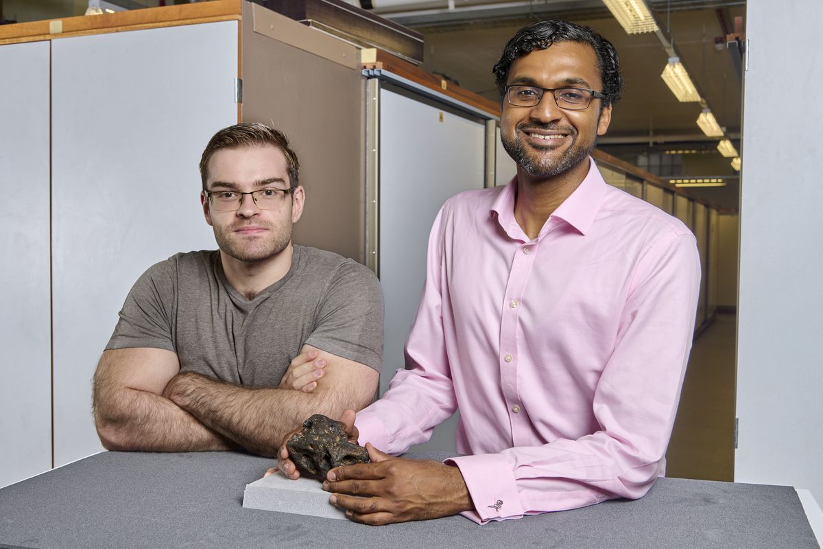 Paleontologists Cassius Morrison and Charlie Scherer at a table with the Invictibellatrix fossil in a museum collection room