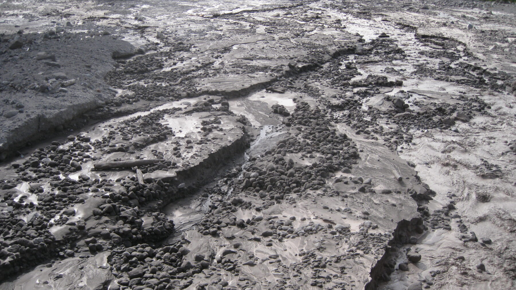 Muddy riverbed on Mount Hood's White River covered with fresh debris-flow deposits of grey mud and rounded cobbles, seen from the Highway 35 bridge
