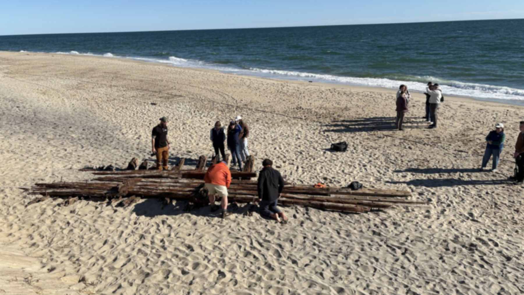 People inspect the timbers of a shipwreck section exposed on a Nantucket beach