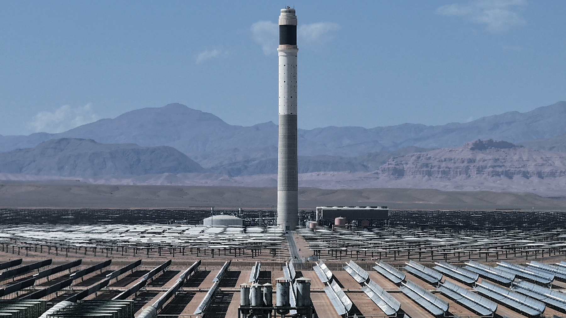 Solar tower of the Noor solar complex rising behind rows of curved trough mirrors near Ouarzazate, Morocco