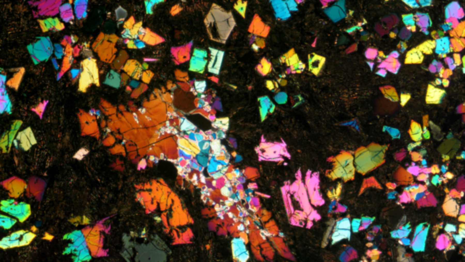 Angrite meteorite NWA 12774 under cross-polarized light, with bright multicolored crystals in a dark groundmass