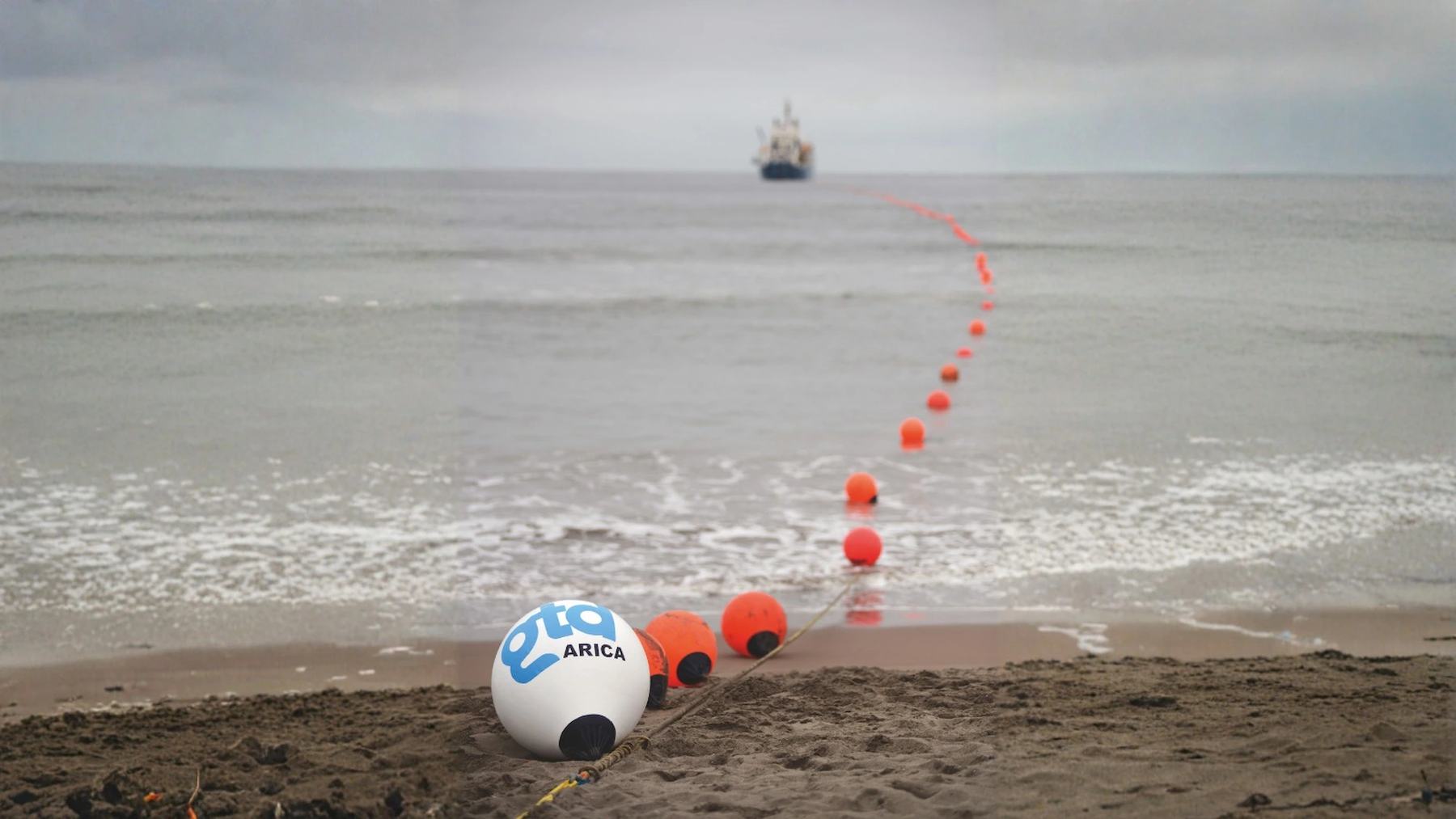 Buoys carrying the Prat undersea internet cable ashore on a beach in Arica, Chile, with a ship offshore
