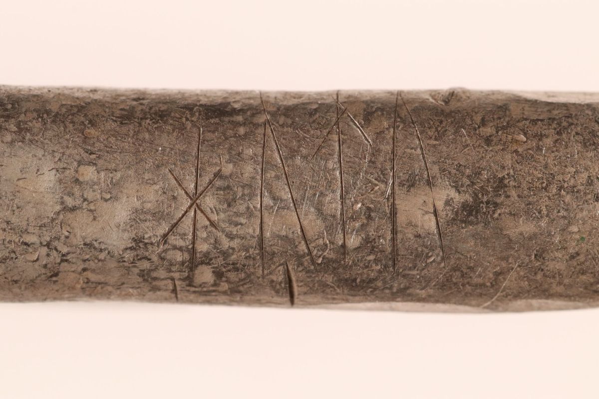Close-up of a worn silver bar with runic letters scratched into its surface