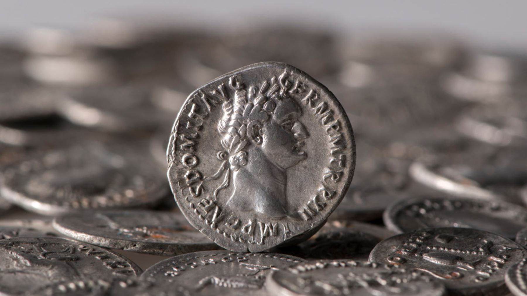 A silver denarius of Emperor Domitian standing upright among the 934 Roman denarii of the Wesseling hoard