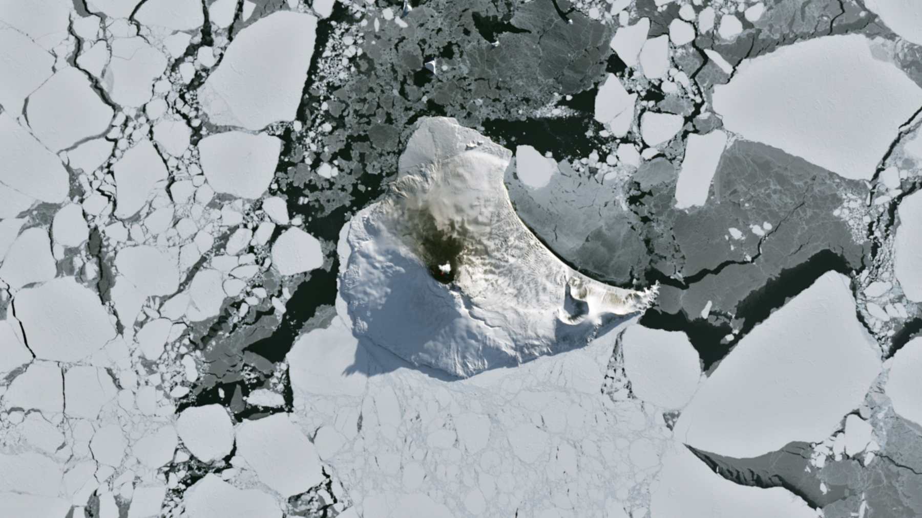Saunders Island surrounded by sea ice, with the lava lake of Mount Michael marked by a small red heat signal and a plume over the summit