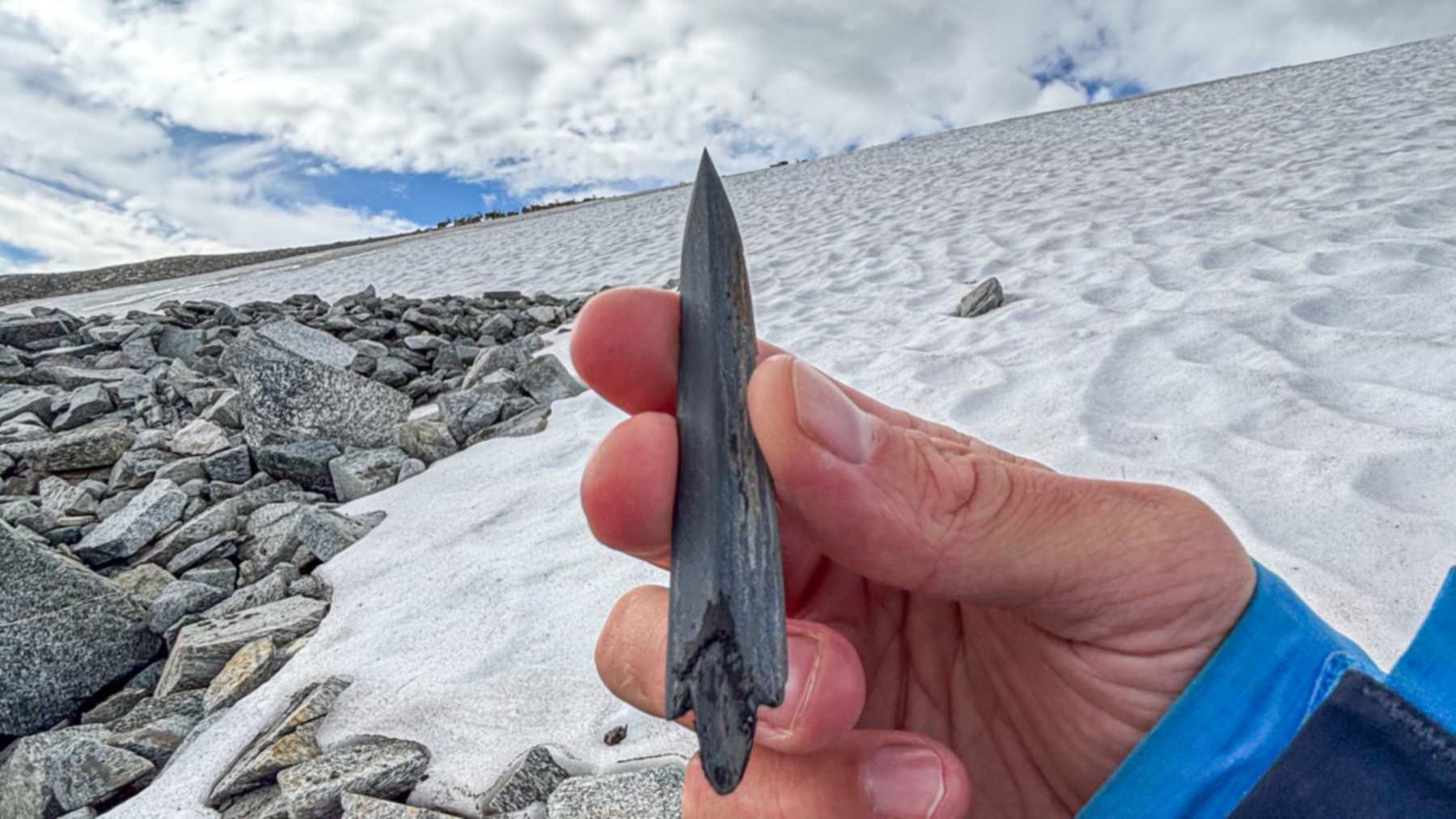 A slate arrowhead estimated at 5,000 to 6,000 years old with reindeer on the ice patch behind it in Norway