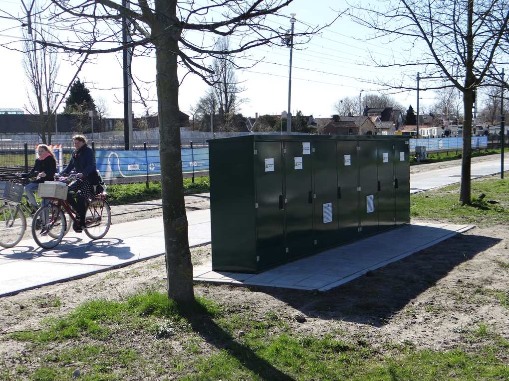 A dark green equipment cabinet beside the SolaRoad solar bike path in Krommenie as two cyclists pass