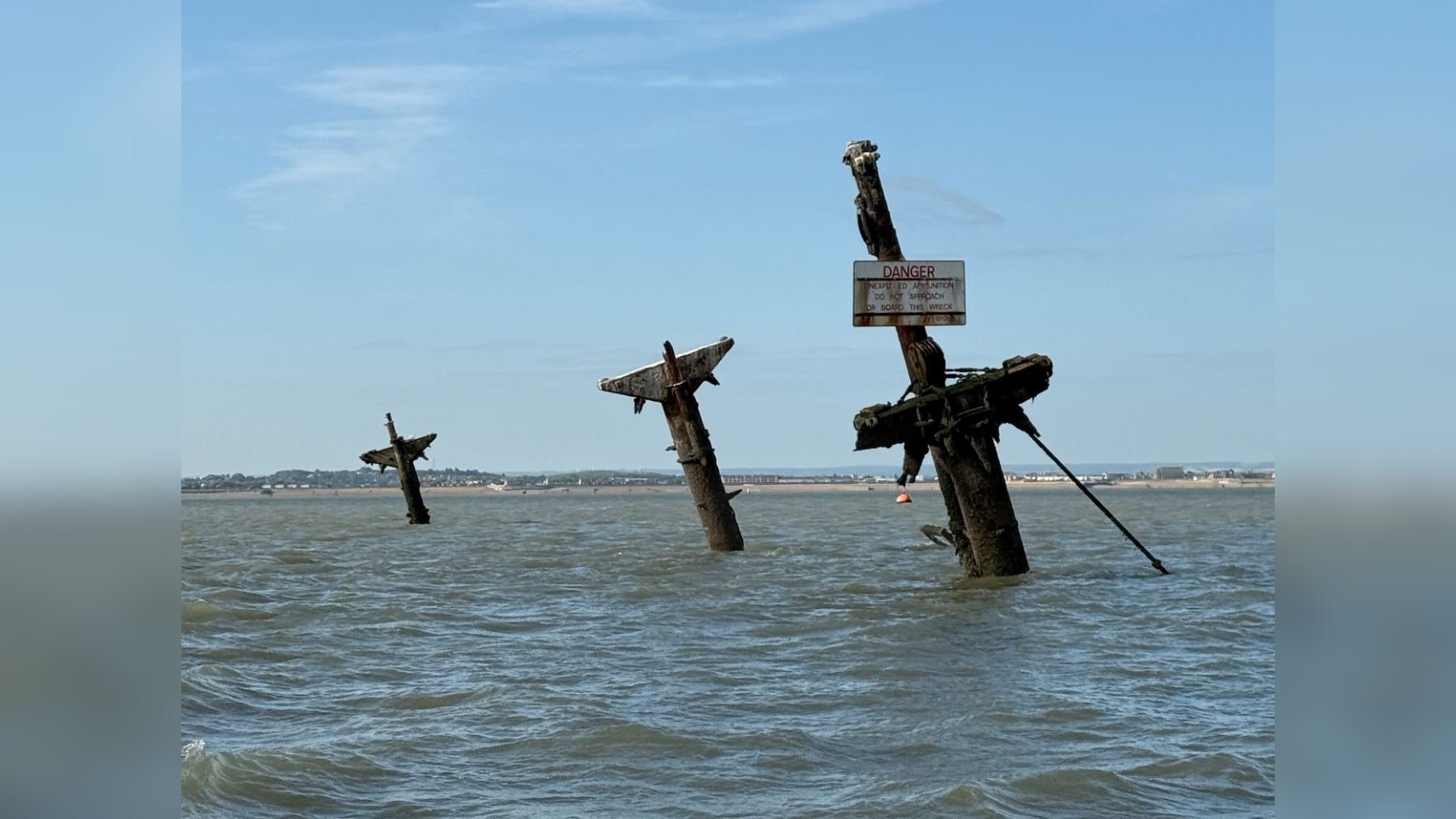 The three masts of the SS Richard Montgomery wreck rising from the Thames Estuary off Sheerness at low tide, with a danger sign warning of unexploded ammunition