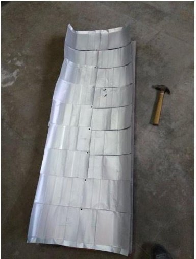 A long panel of opened Tetra Pak cartons stapled together, lying on a concrete floor next to a hammer