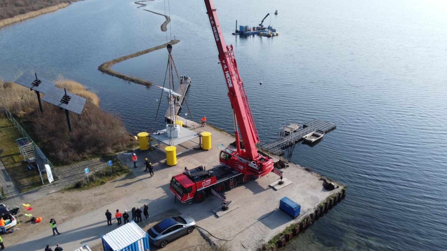 Crane lowering a floating wind turbine with a tilting rotor onto a Dutch lake