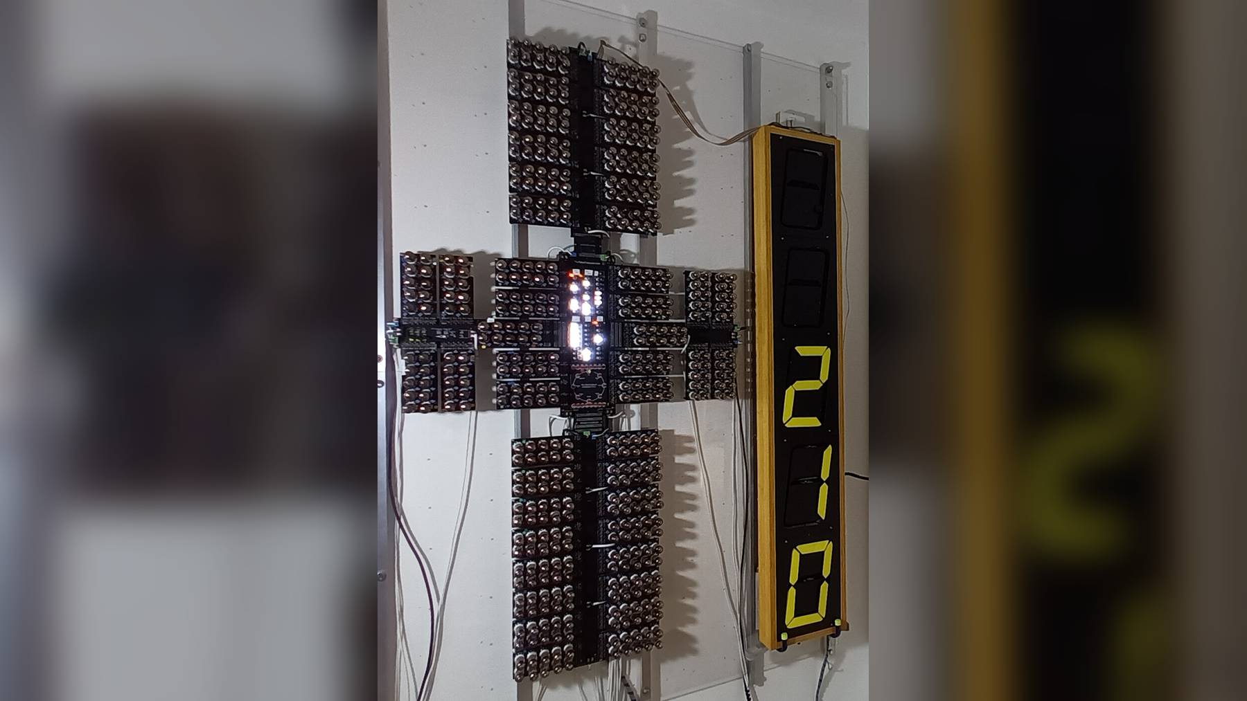 A wall-mounted computer built from hundreds of vacuum tubes arranged in a cross shape next to a tall yellow numeric display
