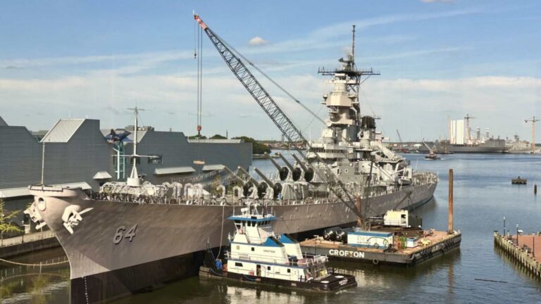 Battleship Wisconsin at its Norfolk pier with the Crofton tug Huntsman at the bow and a Crofton crane barge alongside