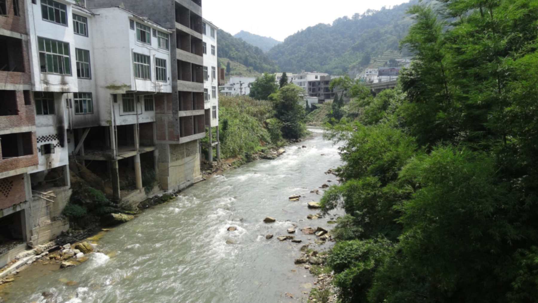 Multistory buildings on concrete pillars line a mountain river in Yanjin County, Yunnan, home of the so-called world’s narrowest city