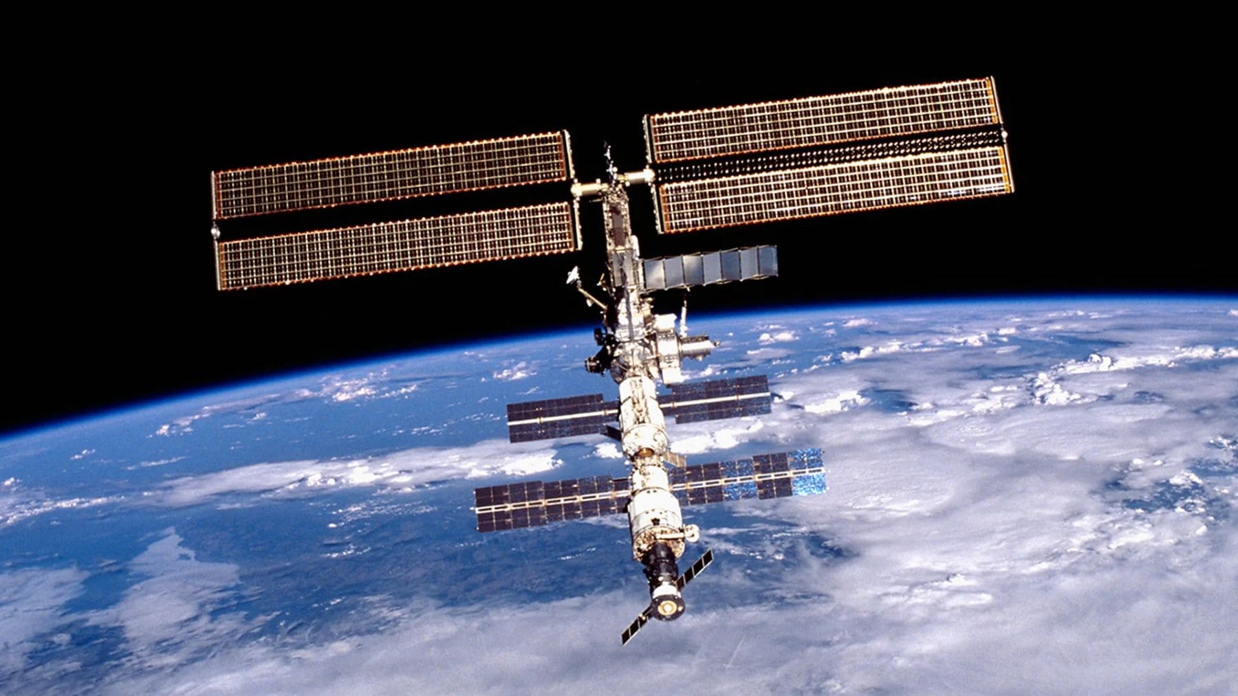 Estación Espacial Internacional (ISS) en órbita sobre la Tierra, con paneles solares desplegados y el planeta al fondo.