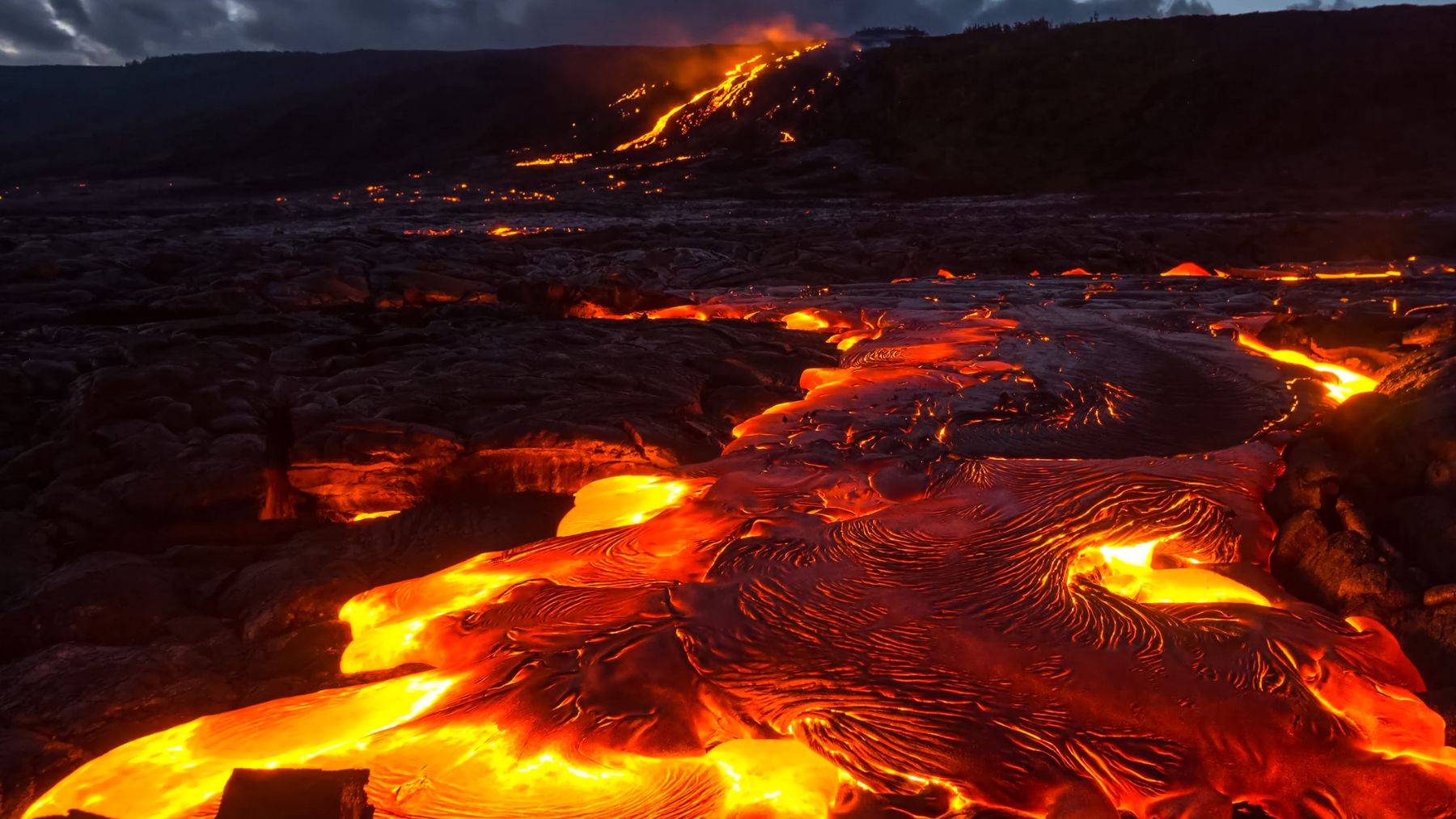 Flujo de lava ardiente descendiendo por la ladera de un volcán activo durante la noche.