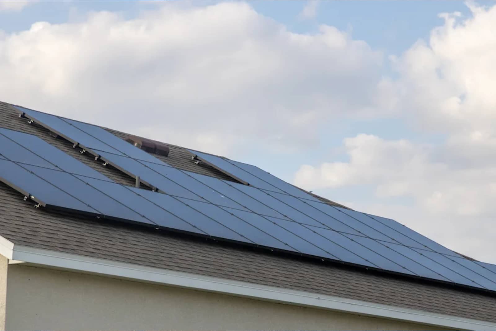 Paneles solares fotovoltaicos instalados en el tejado inclinado de una vivienda bajo un cielo con nubes.