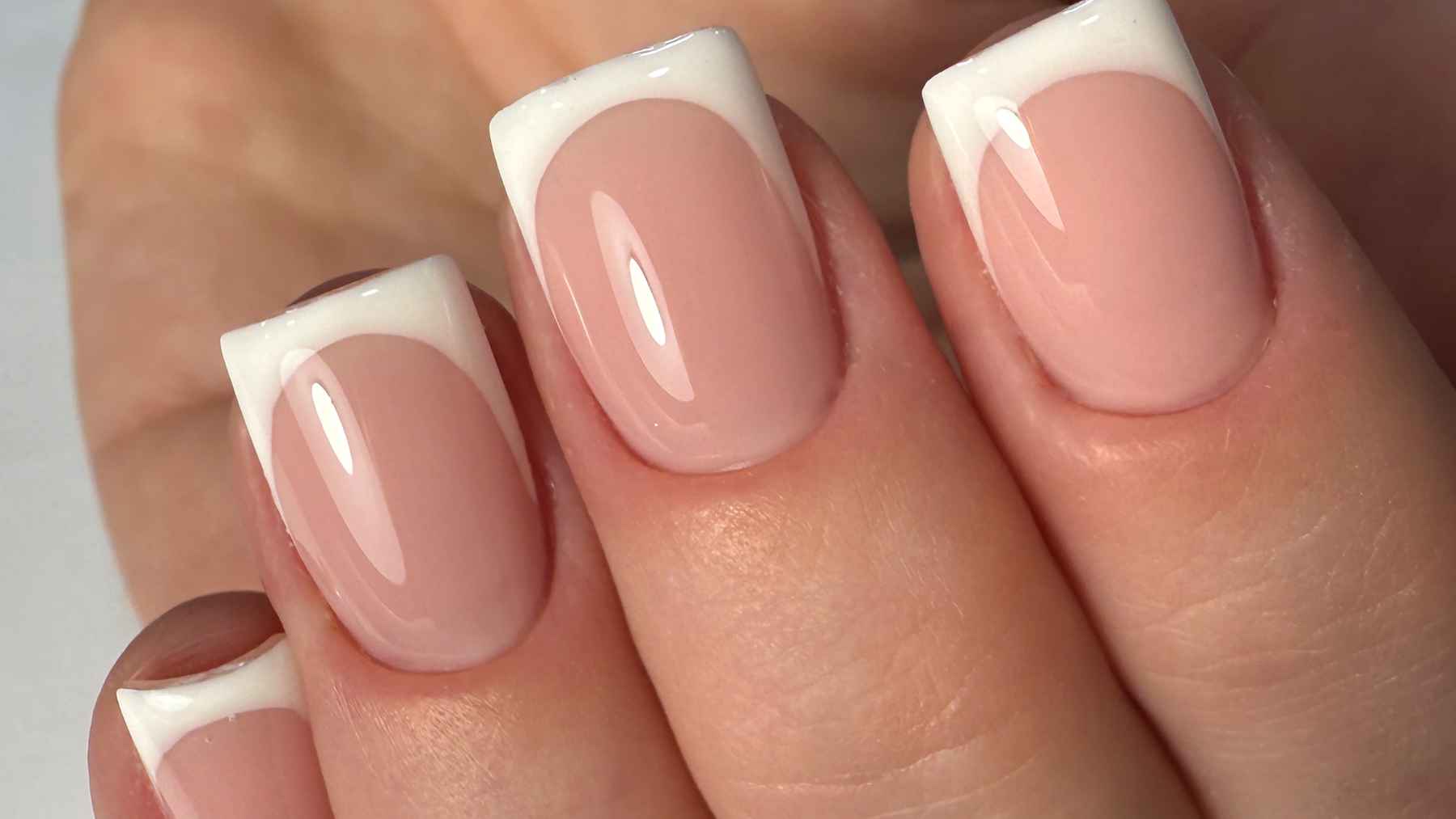 Manicura francesa en uñas naturales con acabado nacarado y brillo, en primer plano