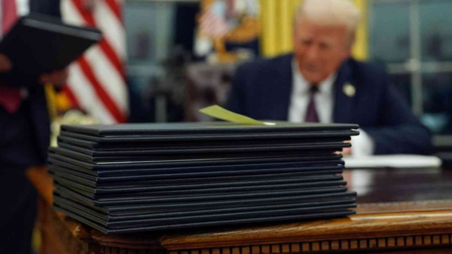 Pila de documentos en la Oficina Oval con presidente trabajando en segundo plano