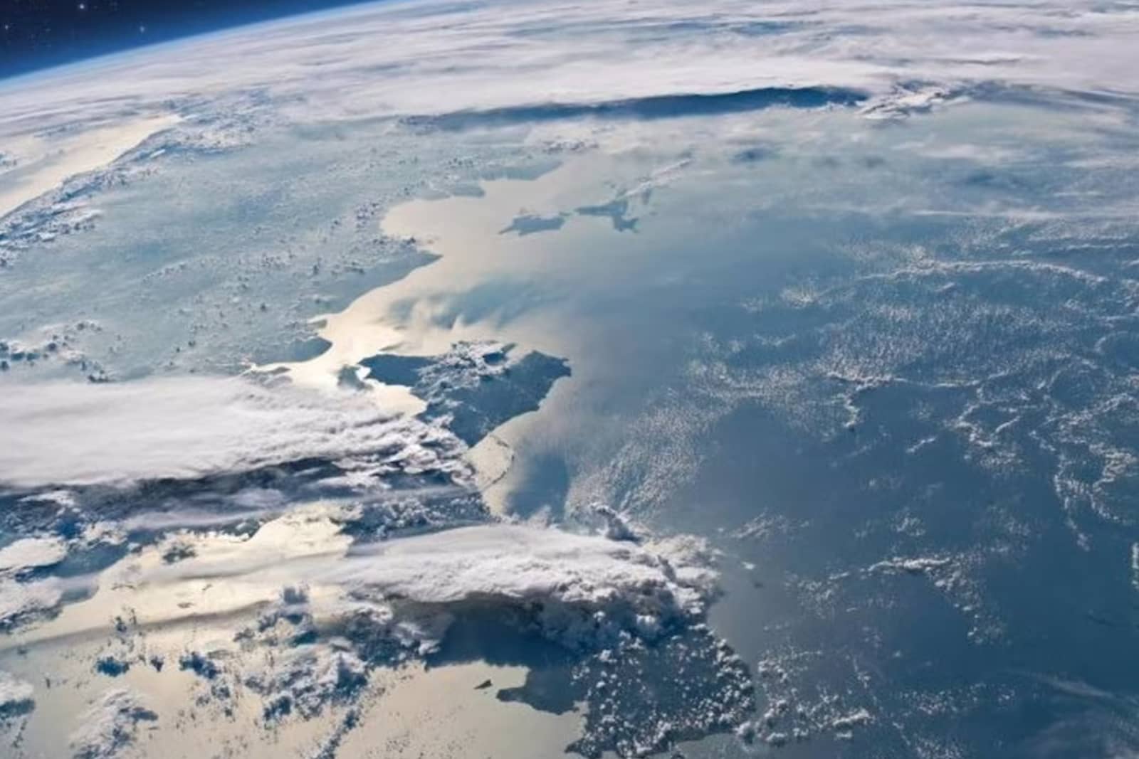 Vista de la Tierra desde el espacio con océano, capas de nubes y el borde de la atmósfera en el horizonte.