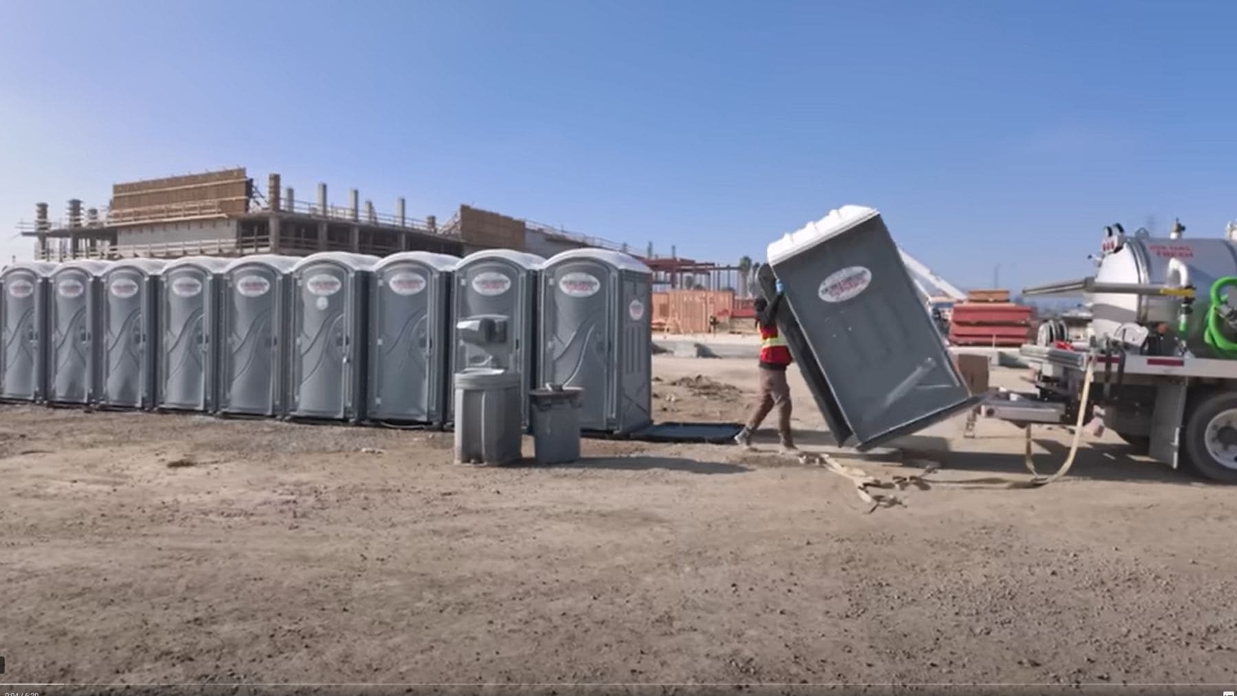 Operario moviendo baños portátiles junto a camión de succión en obra en San Francisco.