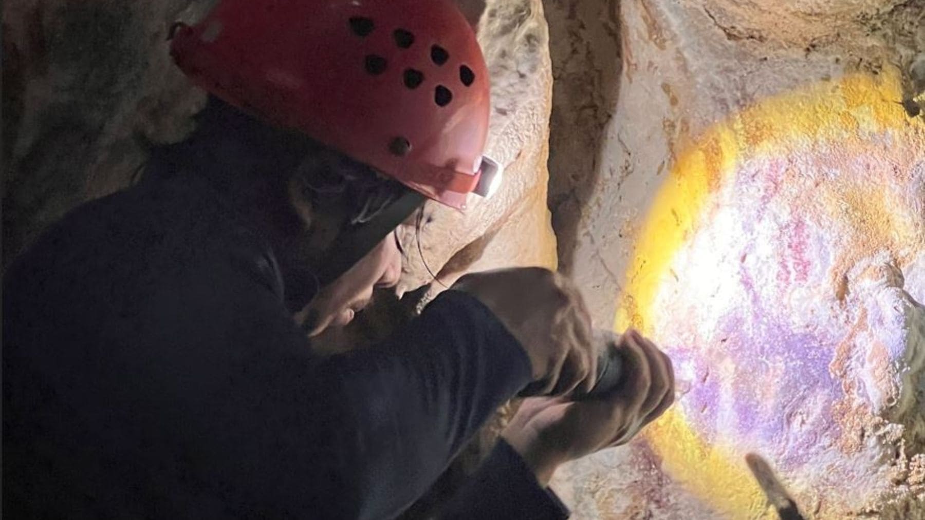 Investigador examina arte rupestre prehistórico en una cueva de Indonesia iluminando un negativo de mano cubierto por calcita.