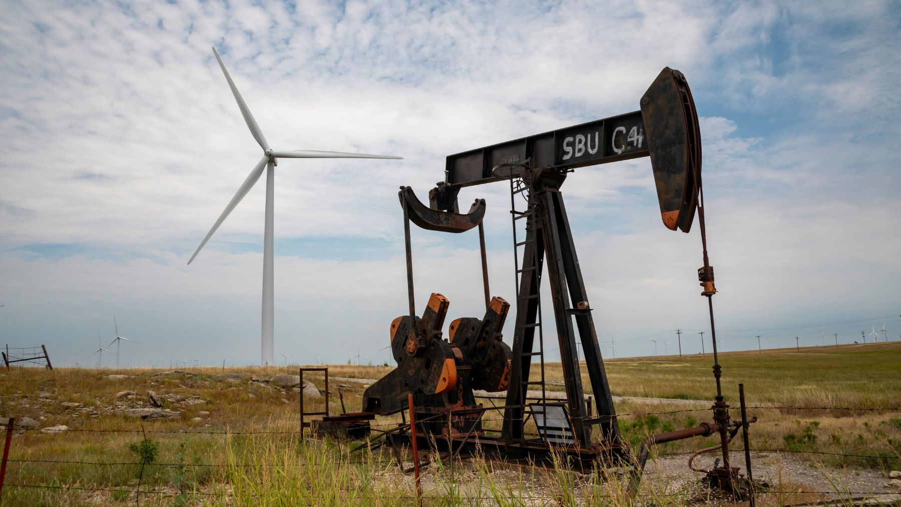 Pozo de extracción de gas con aerogenerador en Australia simbolizando el conflicto entre energías fósiles y renovables.