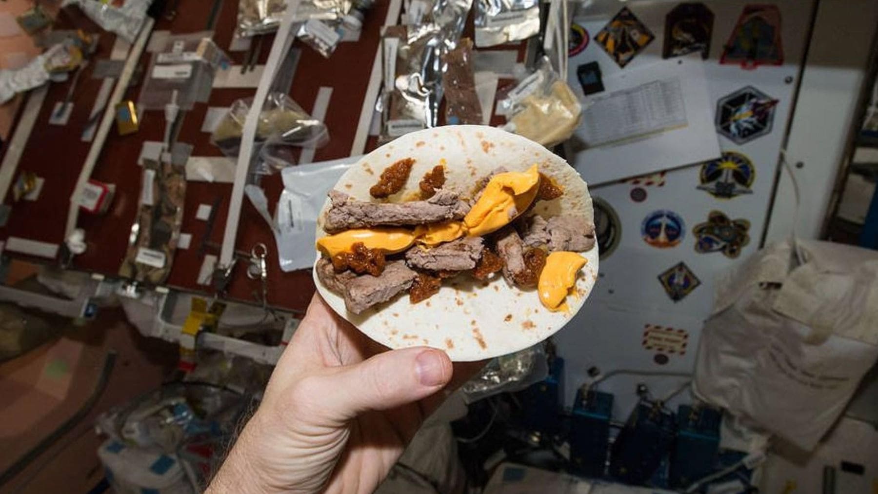 Astronauta sosteniendo comida en microgravedad dentro de la nave con menú espacial de la NASA para Artemis II.
