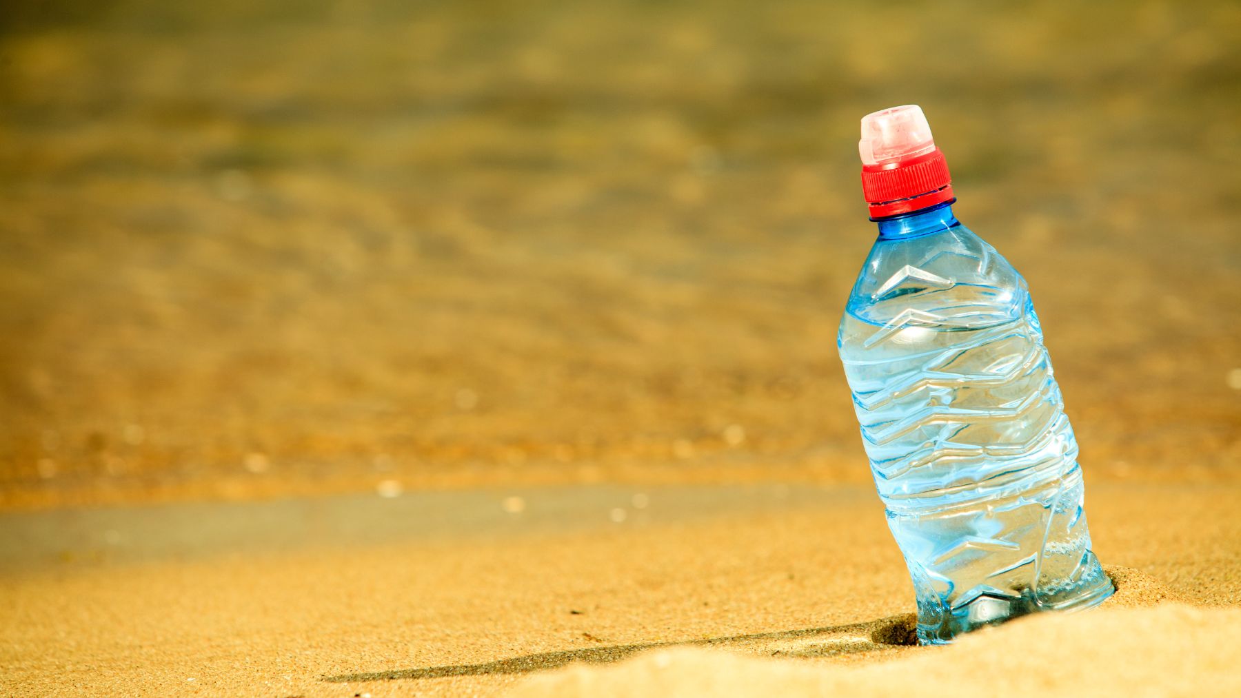 botella de plástico en la arena de una playa relacionada con reciclaje y conversión de botellas en arena reciclada.