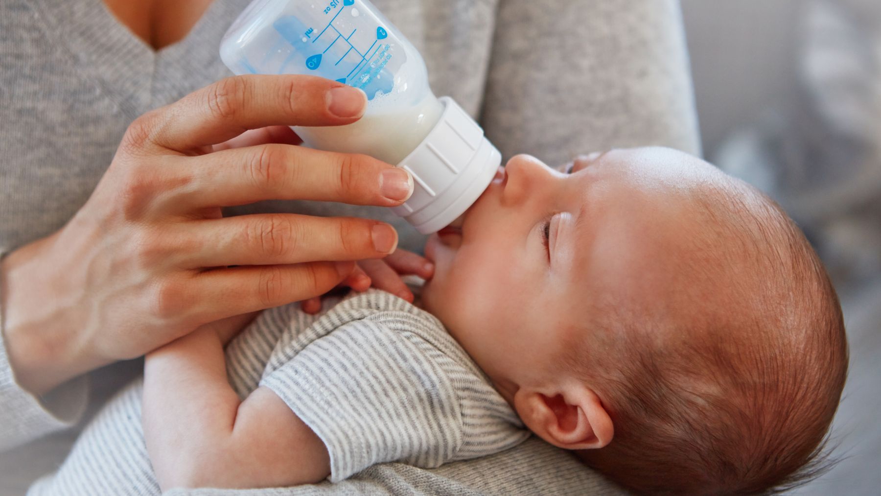 Bebé alimentándose con biberón en brazos de su madre, relacionado con el desarrollo cognitivo infantil y la herencia de la inteligencia.