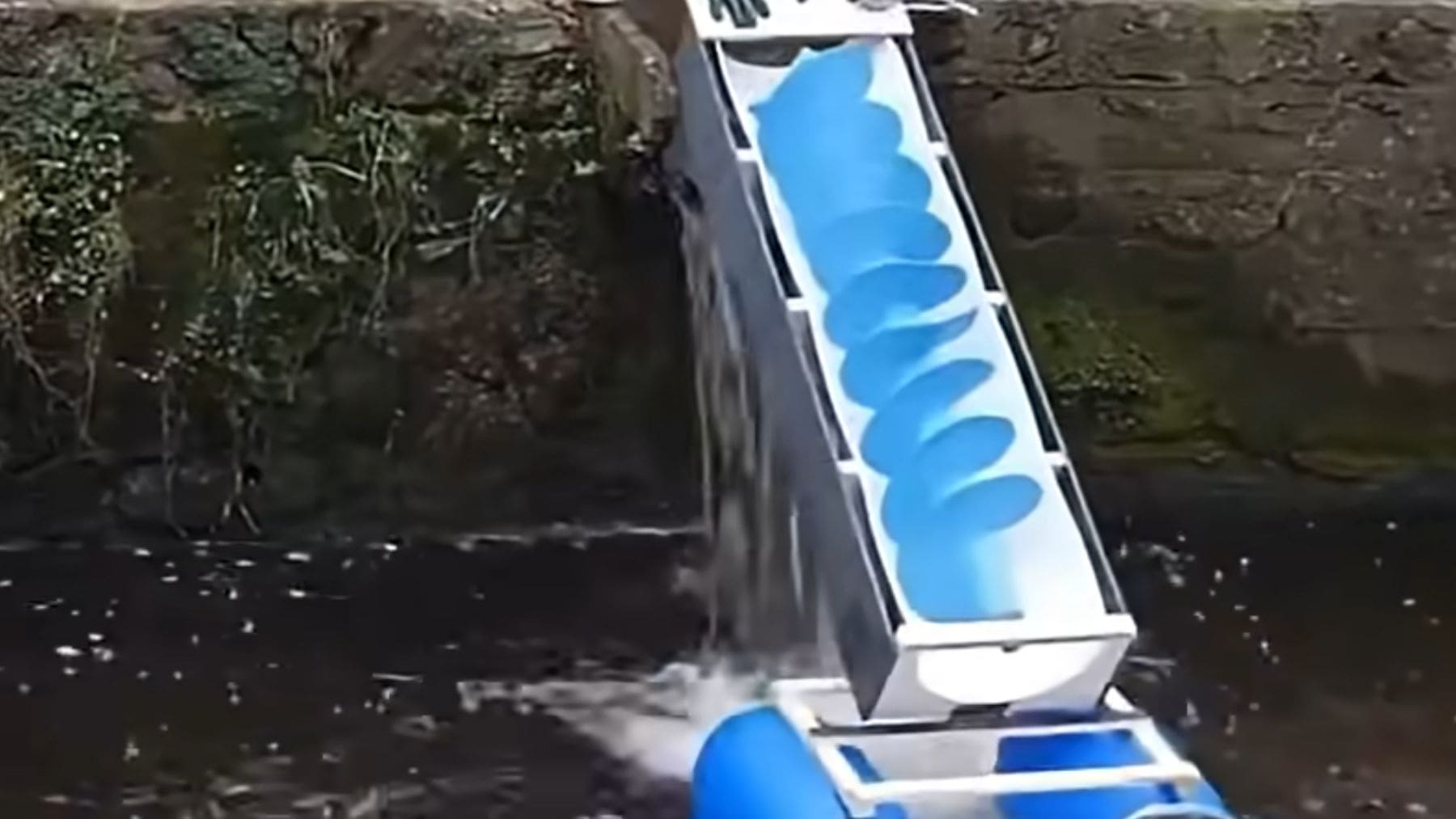 Microcentral hidroeléctrica casera generando electricidad con agua en un canal doméstico.