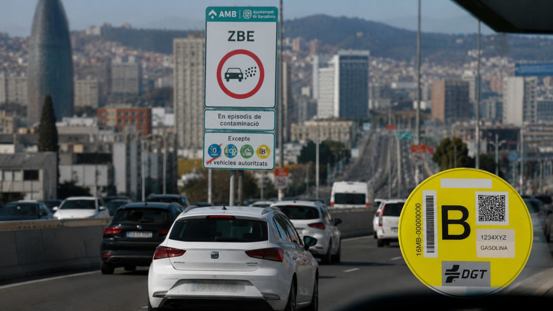 Coches circulando junto a una señal de la ZBE de Barcelona y una etiqueta B de la DGT