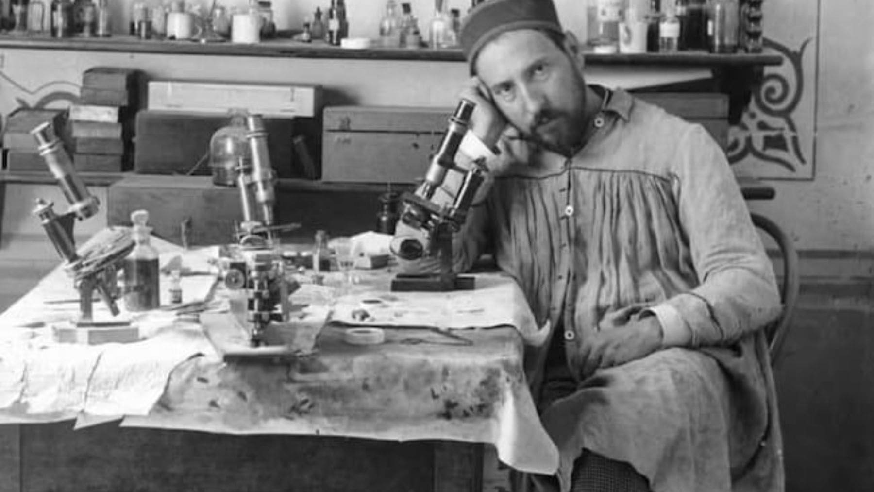 Santiago Ramón y Cajal sentado en su laboratorio junto a varios microscopios.