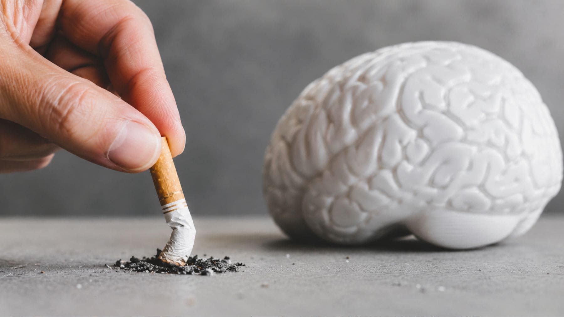 Mano apagando un cigarrillo junto a un cerebro, imagen que ilustra la relación entre dejar de fumar y el riesgo de demencia.
