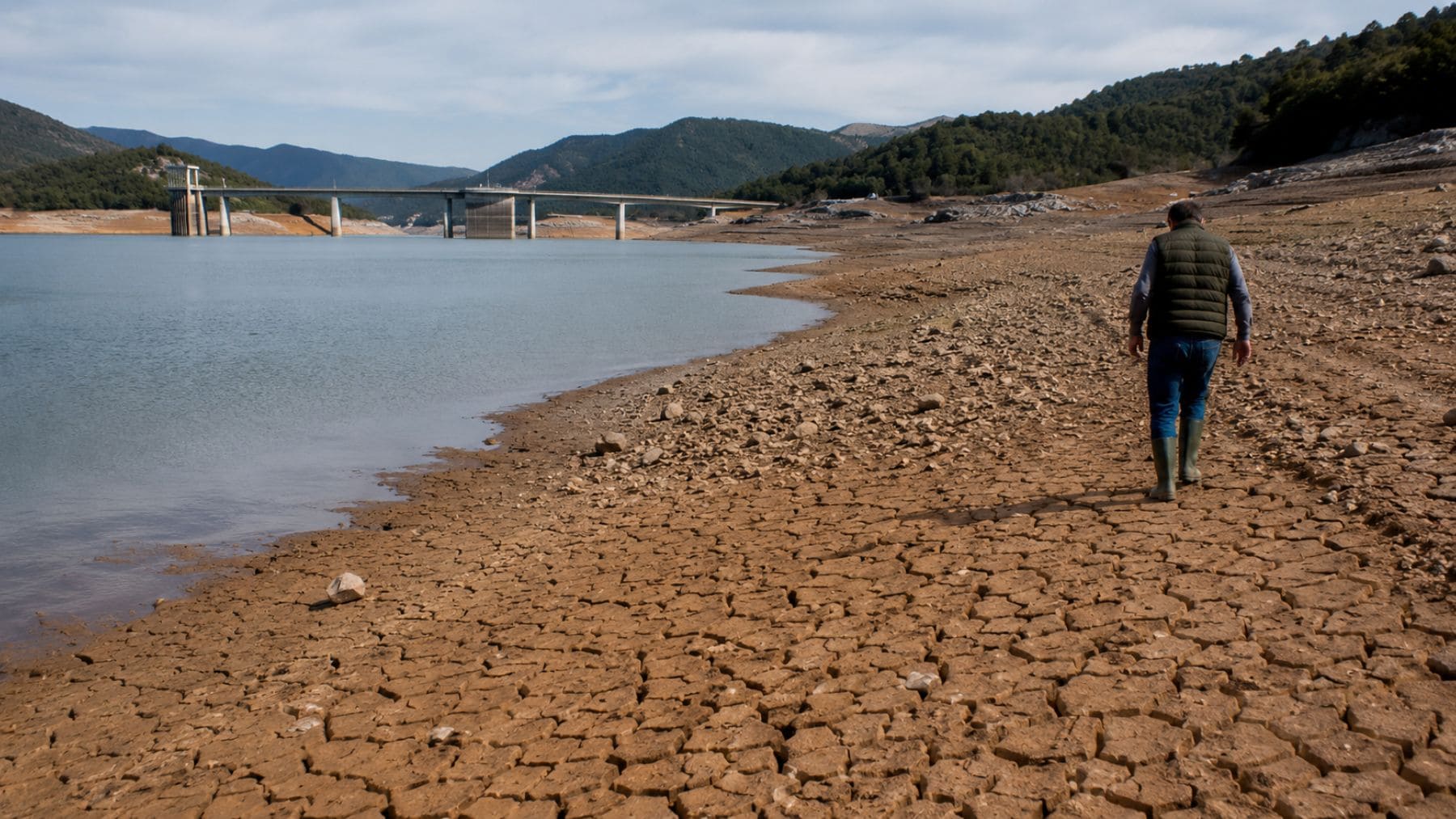 Agricultor junto a un embalse en España con niveles altos de agua y riesgo para los cultivos por el efecto rebote hídrico.