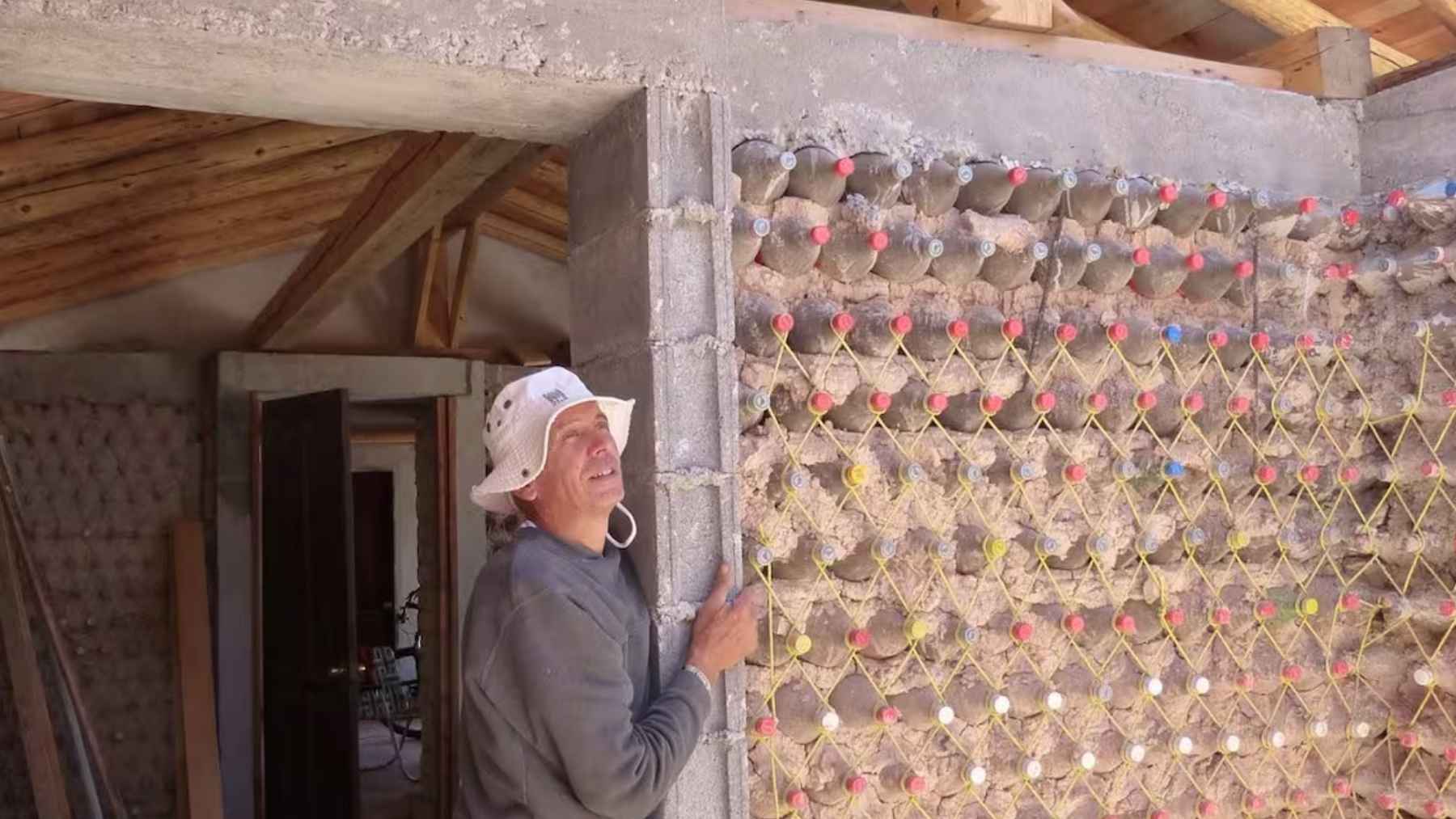 Constructor junto a un muro hecho con botellas de plástico rellenas y unidas con mortero