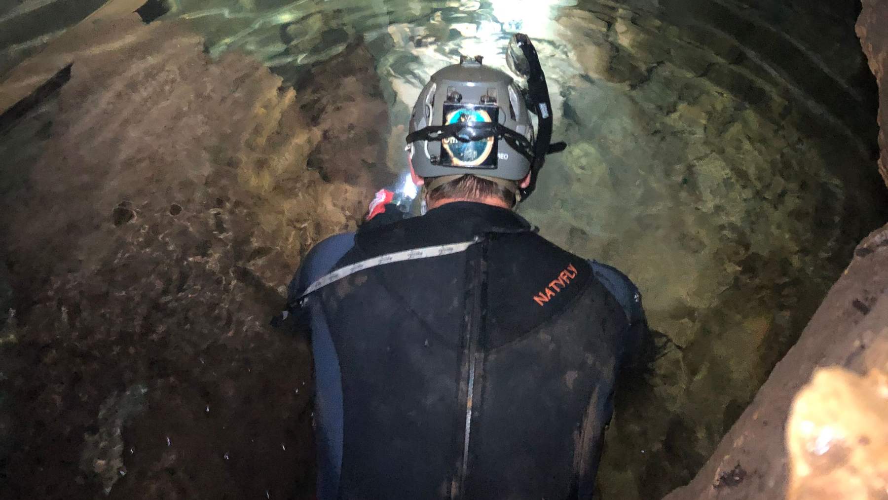El paleontólogo John Moretti, con casco y neopreno, busca fósiles en el arroyo subterráneo de la cueva de Bender, en Texas