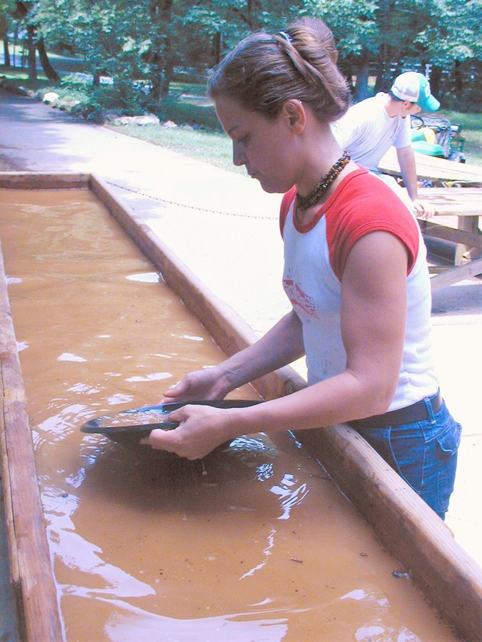 Visitante bateando oro con una batea en un canal de agua de Reed Gold Mine