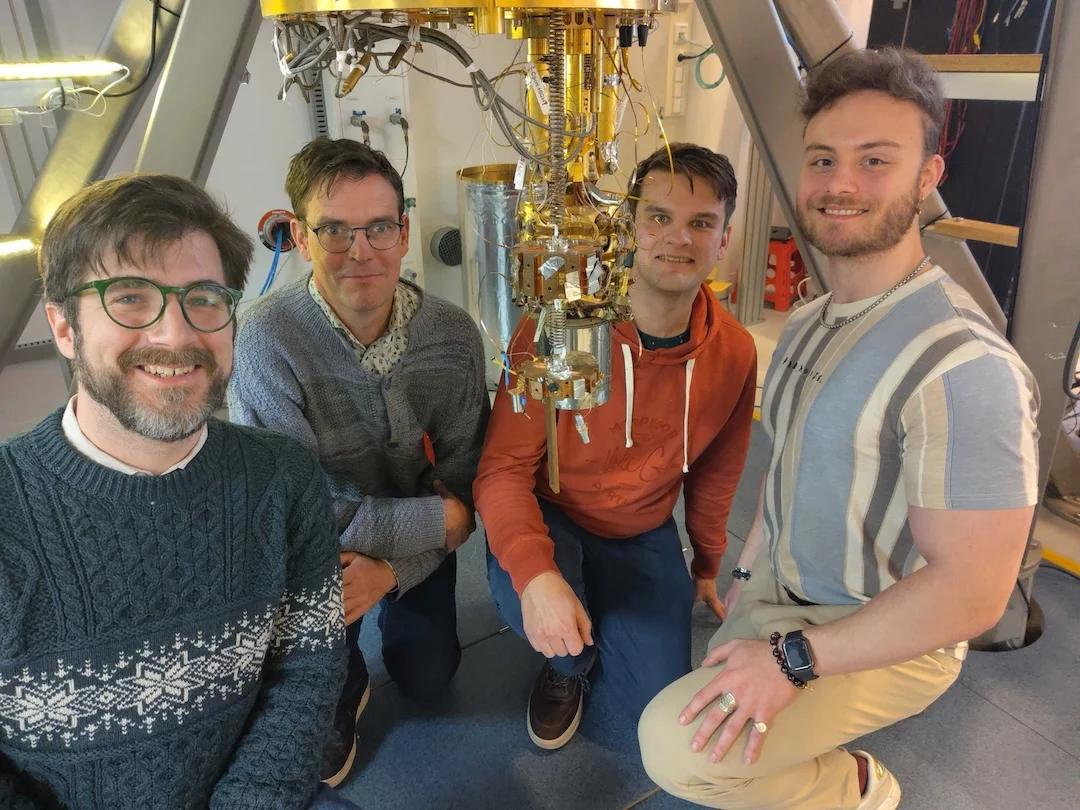 Christopher Tunnell y otros tres miembros del equipo agachados junto a las etapas frías doradas de un criostato