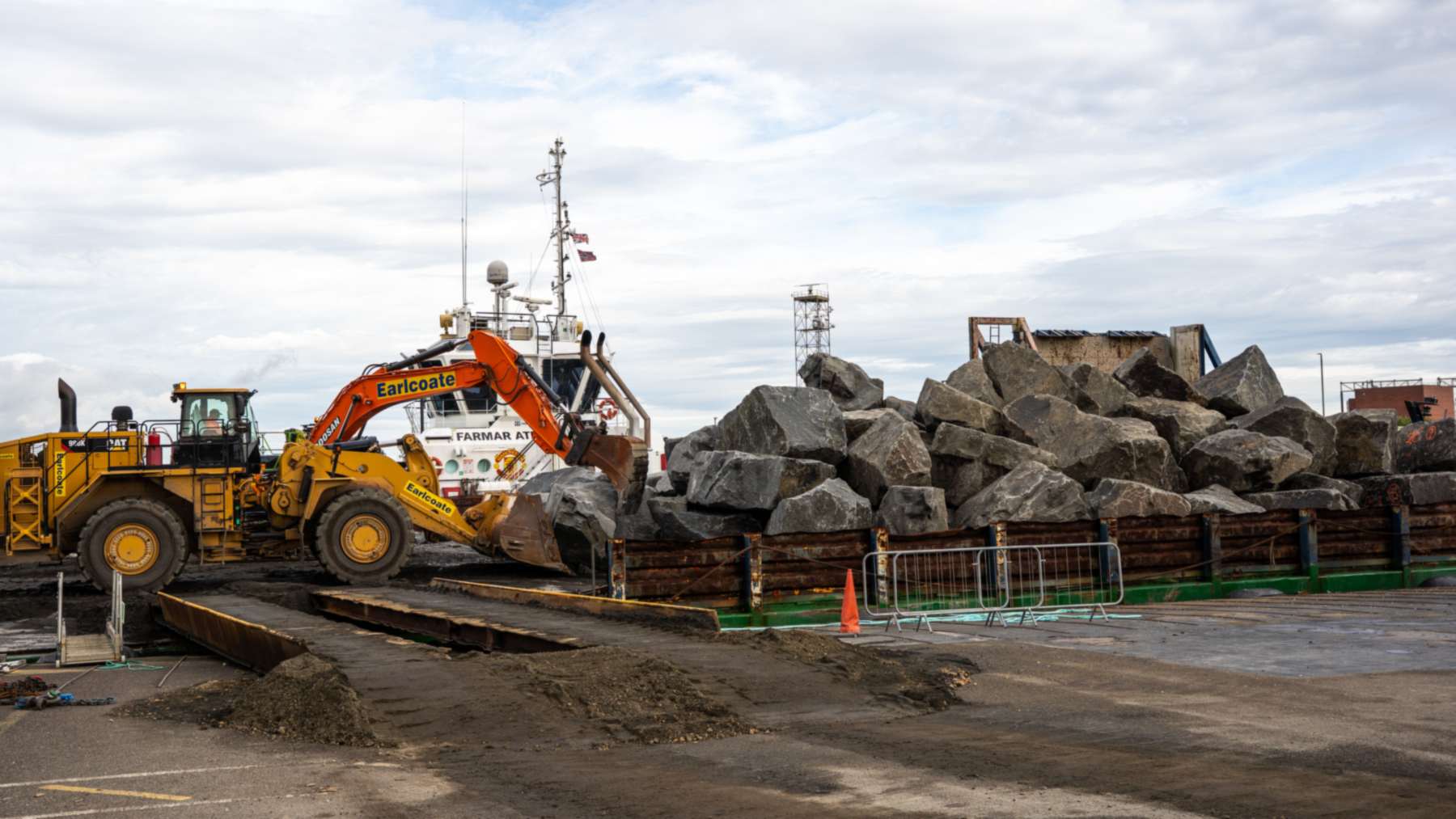 Grandes rocas de granito para el rompeolas de South Gare cargadas en una barcaza junto a una pala cargadora y una excavadora
