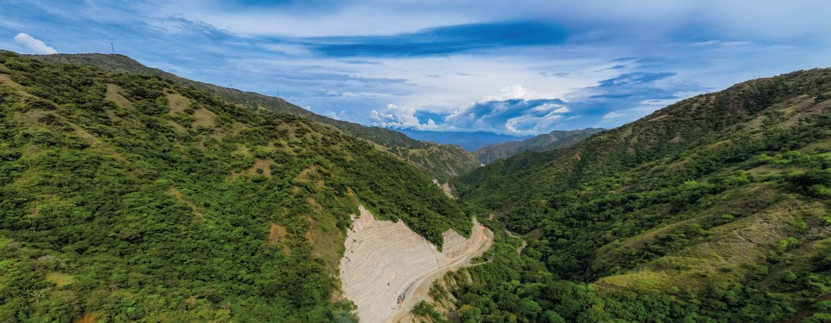 Montañas cubiertas de vegetación del tramo 2 de la Nueva Vía al Mar, con un talud excavado junto a una carretera en obras