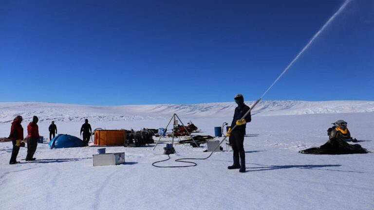 Equipo de perforación con agua caliente sobre el glaciar antártico Langhovde; una persona sosteniendo la lanza, que dispara un chorro de agua caliente al aire