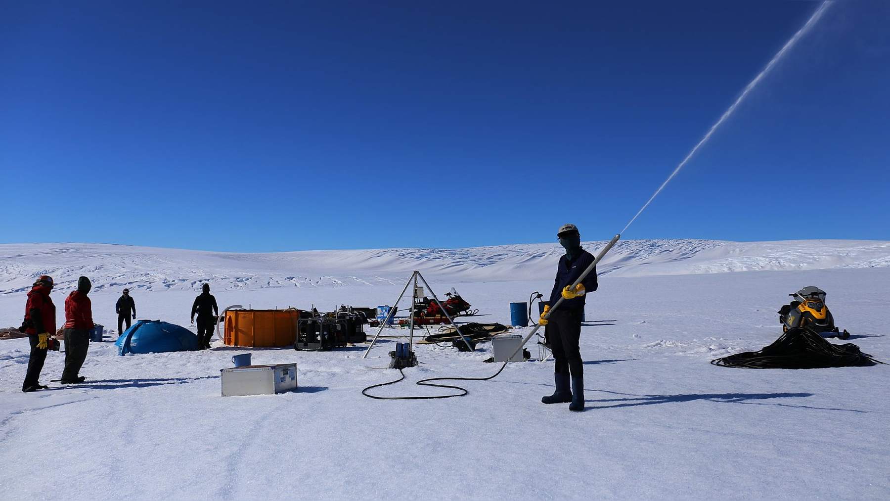 Equipo de perforación con agua caliente sobre el glaciar antártico Langhovde; una persona sosteniendo la lanza, que dispara un chorro de agua caliente al aire