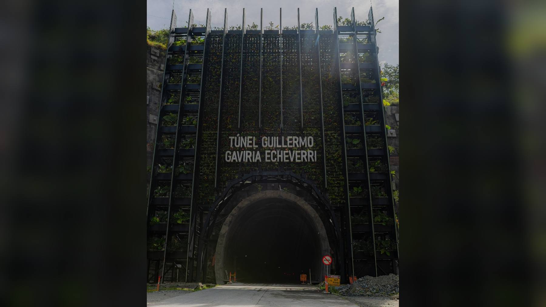 Portal del Túnel del Toyo, con el nombre Túnel Guillermo Gaviria Echeverri sobre una fachada metálica con plantas