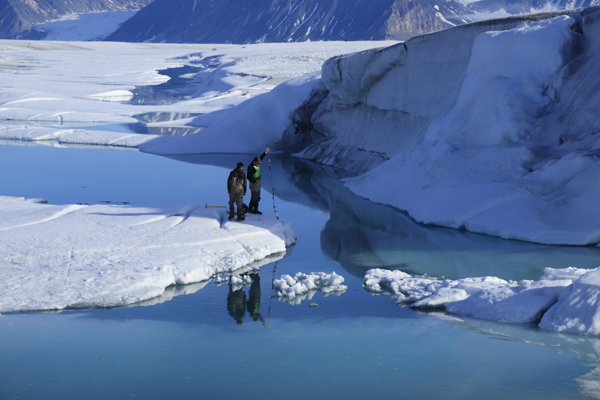 Dos investigadores bajan un instrumento al agua desde el borde del hielo en el fiordo Milne