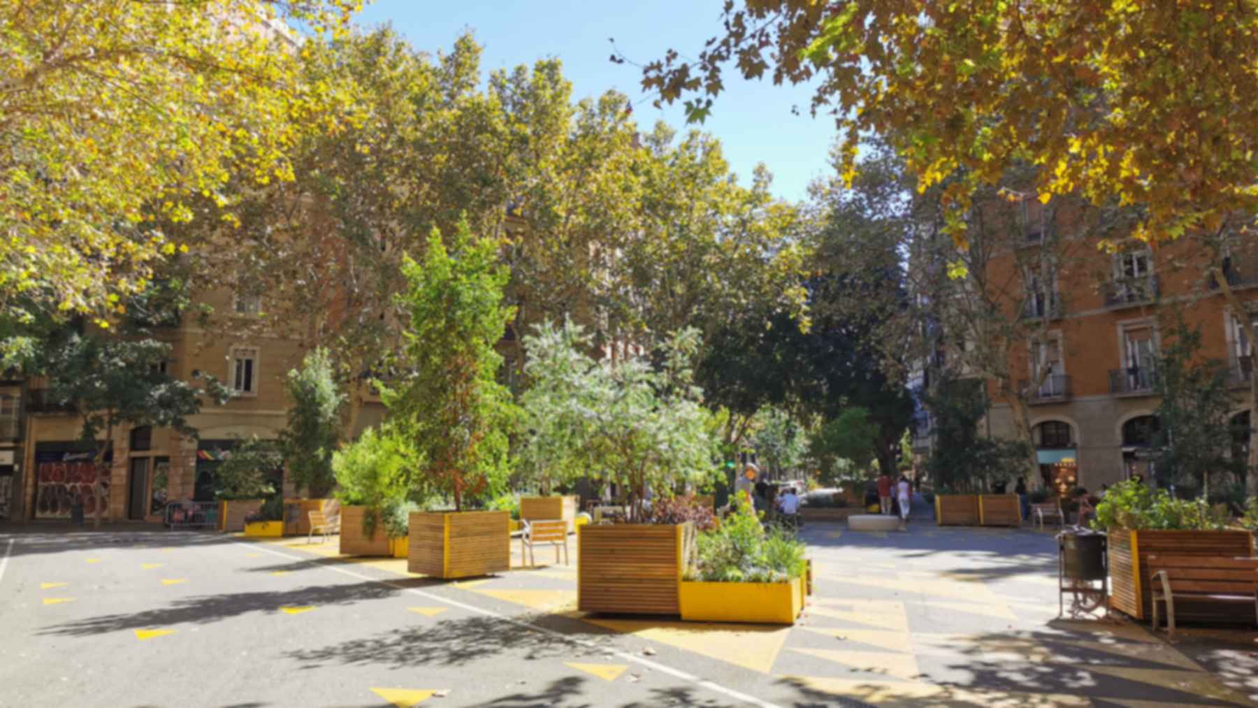 Calle pacificada de las supermanzanas de Barcelona en Sant Antoni, con jardineras de madera, bancos y árboles